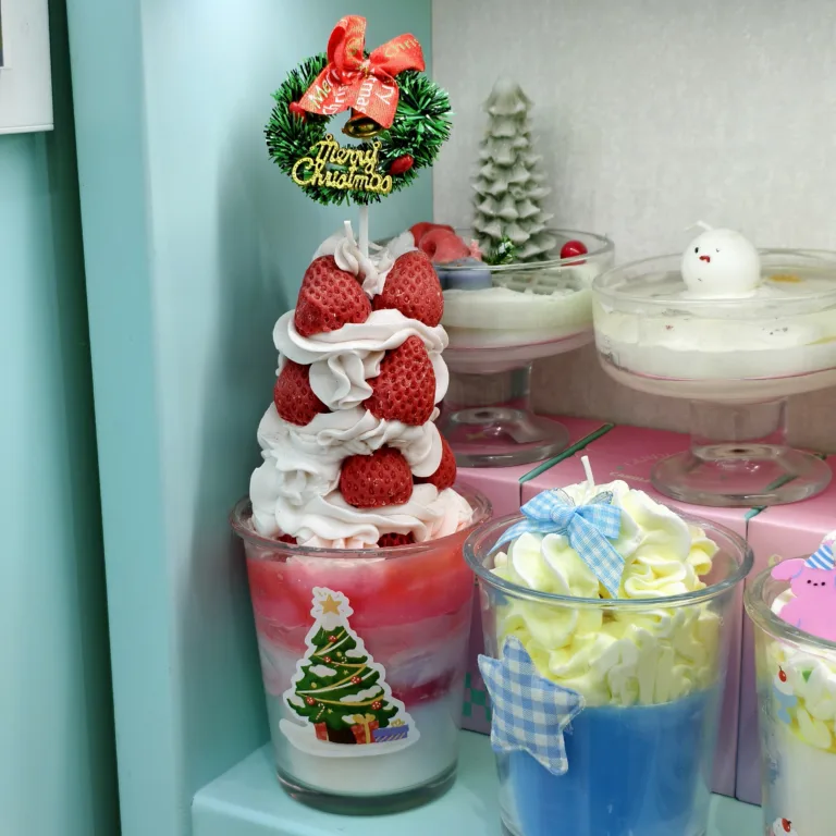 Christmas-themed realistic dessert candles in glass cups, decorated with whipped cream-style wax, strawberries, pastel colors, and festive ornaments.