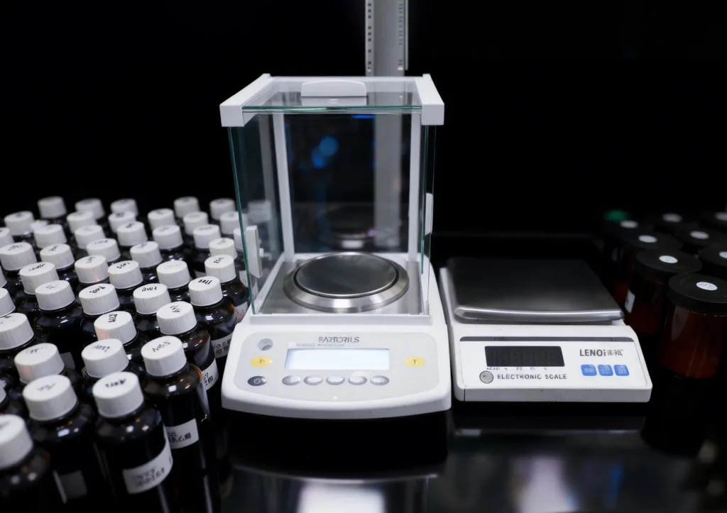 Inside a Professional Candle Fragrance Lab: From Library to Custom Scent 3 Precision electronic balance used in a candle fragrance laboratory, surrounded by labeled fragrance oil bottles and sample containers for formulation and testing.