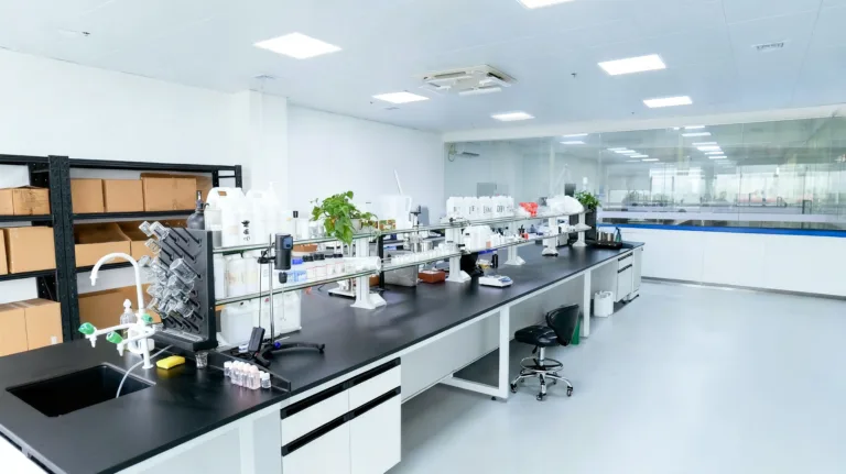 Clean and modern candle fragrance laboratory workspace with testing equipment, formulation tools, and materials arranged on a long workbench for product development.